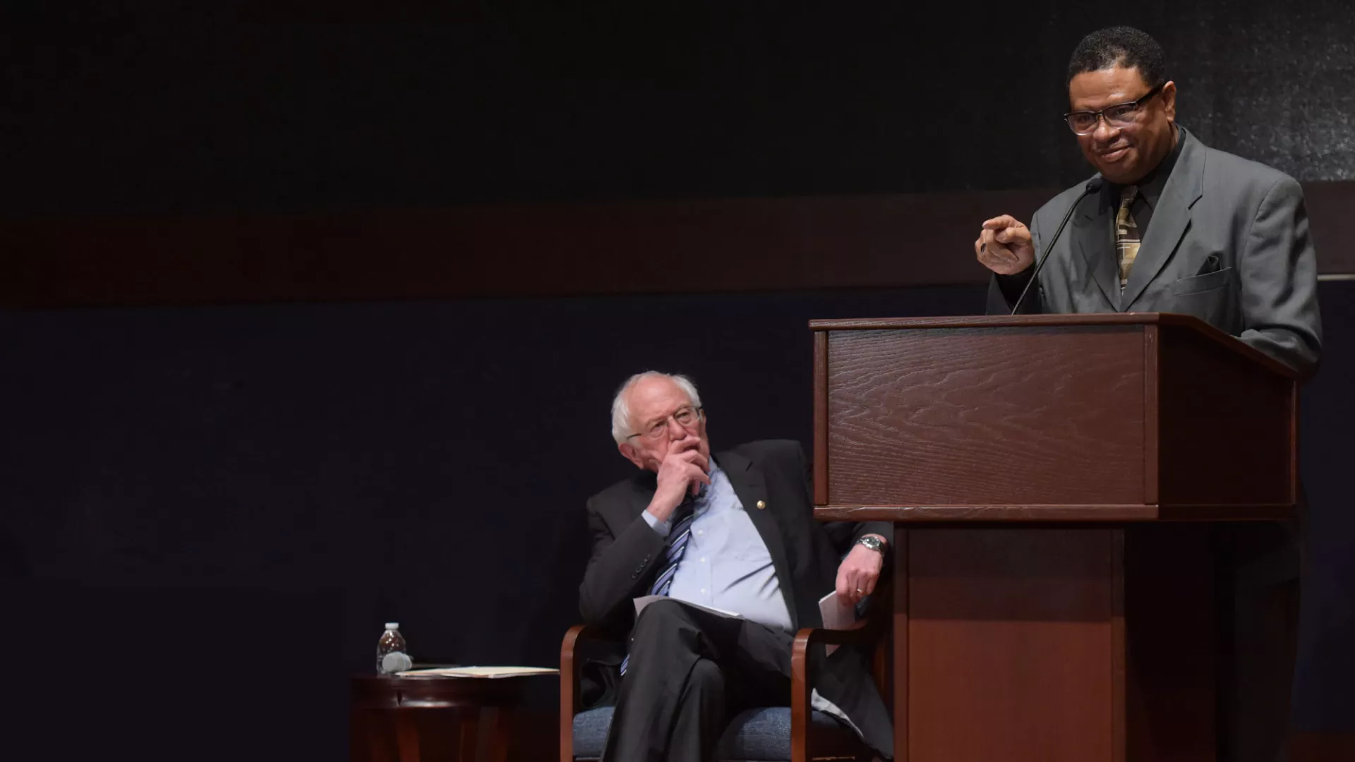 a black man at a lecturn with Sen. Bernie Sanders looking on