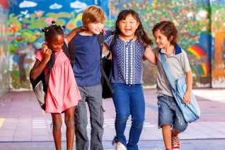 four diverse kids in elementary school lock arms with a colorful mural in the background
