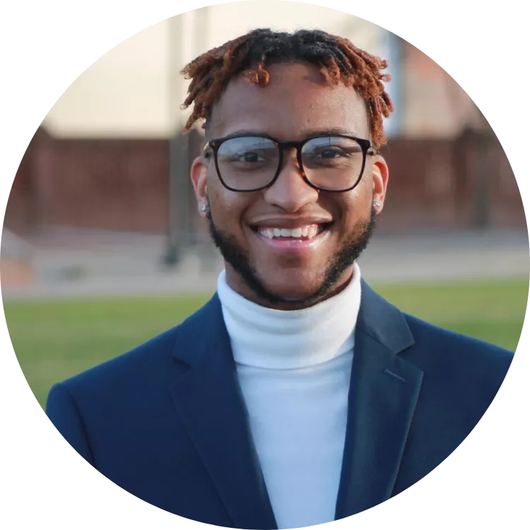 Timothy Lyons smiles for a photo in front of an outdoor athletic field.